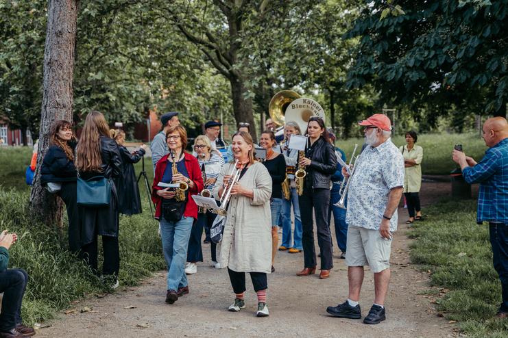 Tag der Nachbarn 2024 Gruppe von Musiker:innen marschiert auf einem Weg, während Zuschauer:innen sie mit Freude beobachten.