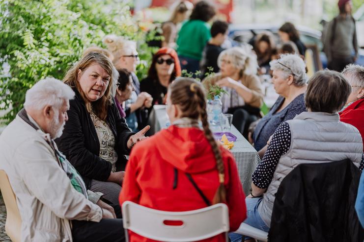 Gruppe von Personen unterschiedlicher Altersgruppen, die sich bei einer offenen Unterhaltung an einem Tisch versammeln.